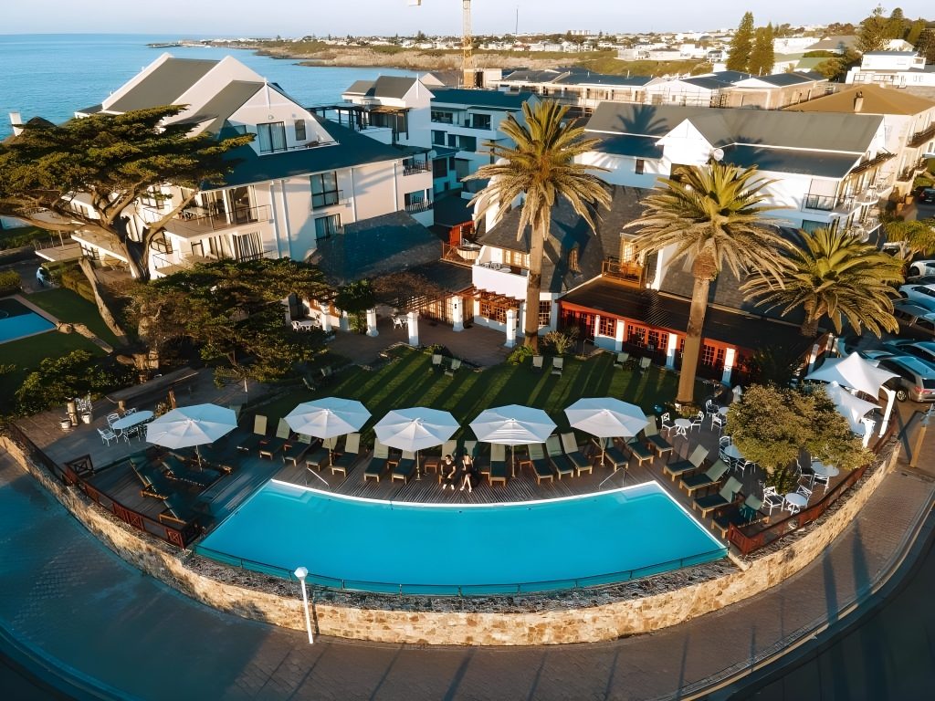 The hotel from the air, with the pool, lawn and palms above the bay