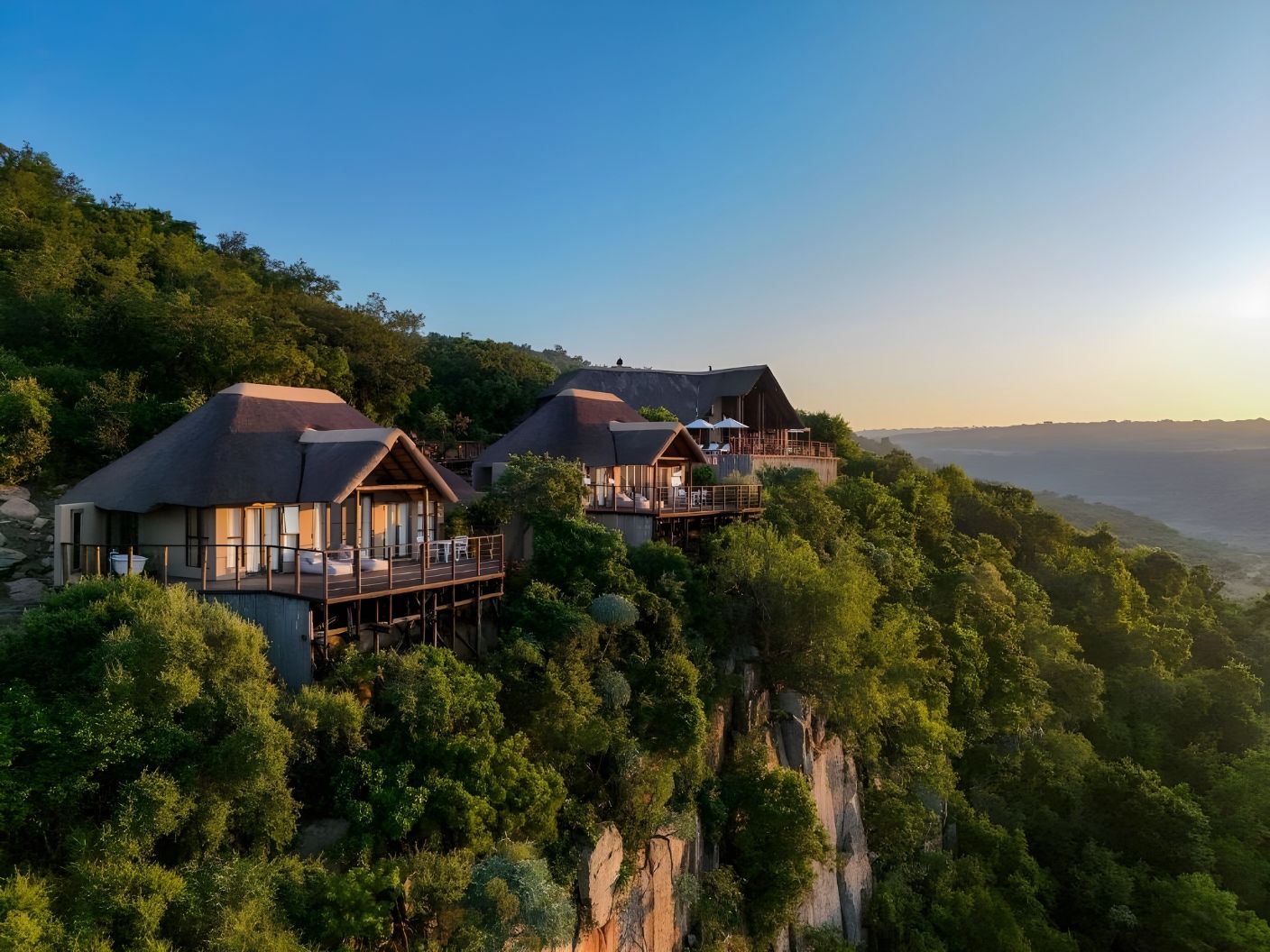Esiweni's thatched suites on the cliff edge at sunrise, above the Nambiti valley